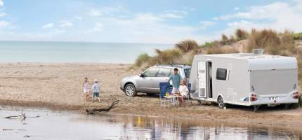 VRK Ausland-Schadenschutz – Eine junge Familie ist mit ihrem Auto und Wohnwagen an einem Strand.