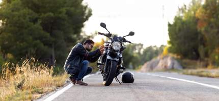 Motoradversicherung – Ein junger Mann steht mit seinem Motorrad auf einem Feldweg.