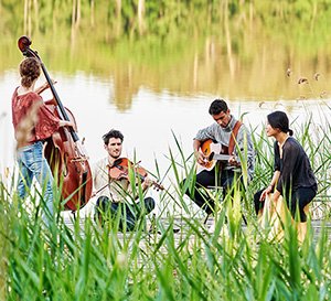 VRK Berufsunfähigkeitsabsicherung – Eine Gruppe junger Menschen sitzt an einem See und spielt auf ihren Instrumenten.