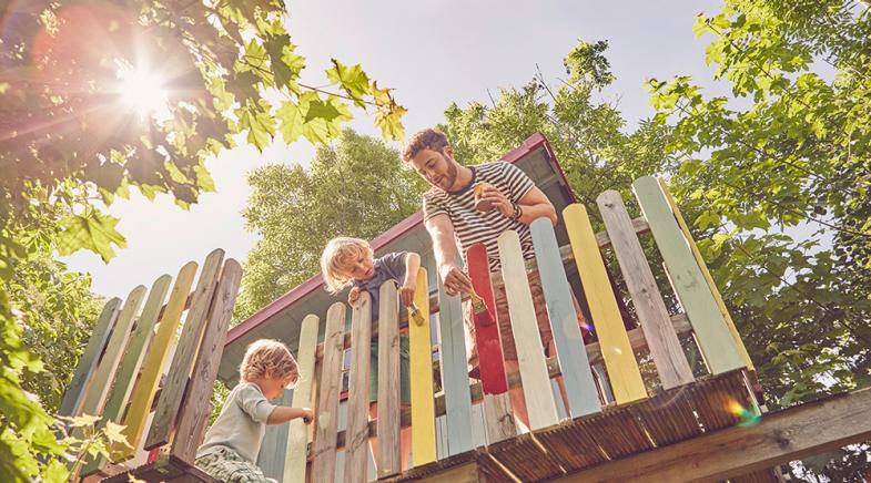 VRK Bauherren-Haftpflichtversicherung – Ein junger Vater streicht mit seinen Söhnen das Baumhaus.