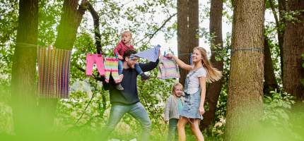 VRK Hausratversicherung – Eine junge Familie hängt zusammen Wäsche im Garten auf.