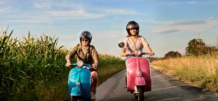 Mopedversicherung – Ein junger Mann fährt mit einer Freundin Mofa.