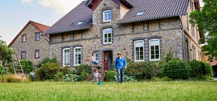 VRK Wohn­gebäude­versicherung – Eine Familie vor einem Wohnhaus