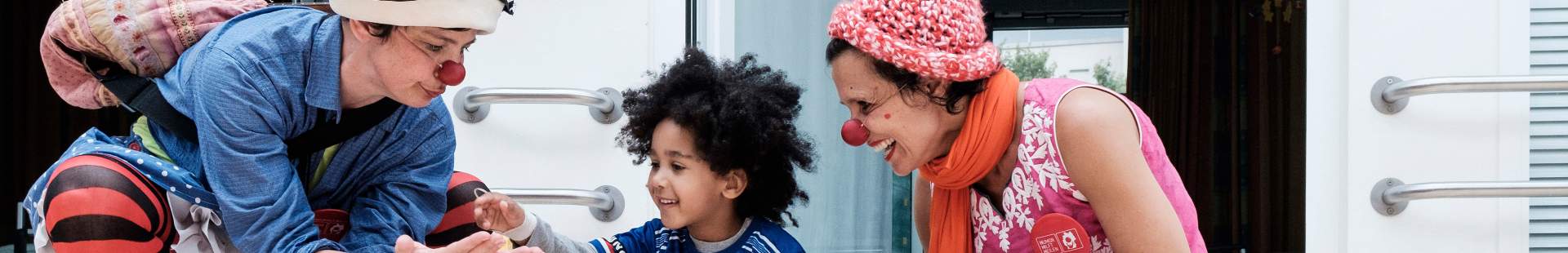 VRK HUMOR HILFT HEILEN – Zwei HHH Clowns spielen mit einem Kind auf dem Boden in der Asklepios Kinderklinik.
