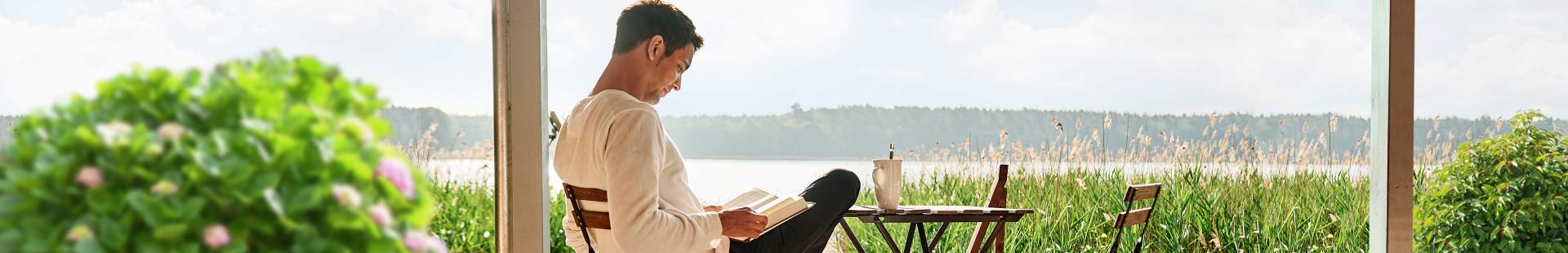 Ein junger Mann sitzt auf seiner Terrasse und liest ein Buch.