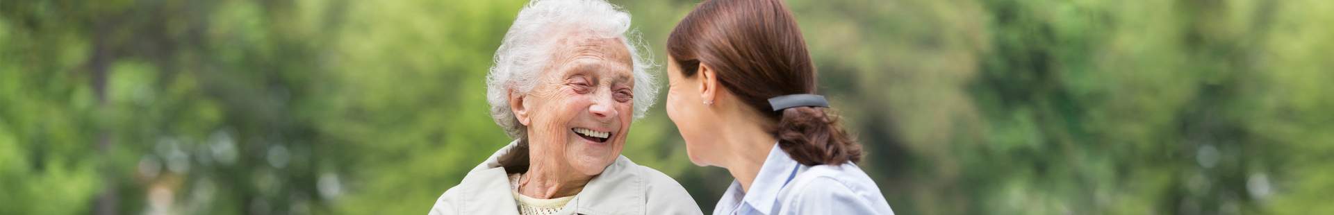 VRK Staatlich geförderte Pflege-Zusatz­versicherung – Eine Seniorin sitzt mit Ihrer Pflegerin auf einer Parkbank.