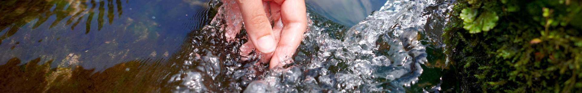 VRK Transparenz – Eine Hand greift in einen Bach mit klarem Wasser.