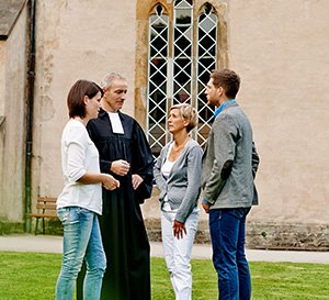 VRK Pfarrer und Kirchenbeamte – Ein Pfarrer unterhält sich mit Kirchenbeamten vor einer Kirche.