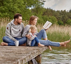 VRK Risiko-Lebensversicherung – Eine junge Familie sitzt zusammen auf einem Steg am See.
