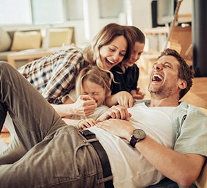 VRK Unfallschutzbrief – Eine junge Familie lacht zusammen im Wohnzimmer.
