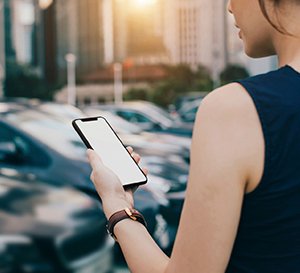 VRK eVB-Nummer – Eine junge Frau steht mit Ihrem Handy vor neuen Autos.