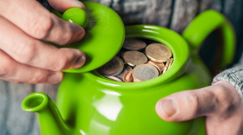 VRK Pflege-Monatsgeldversicherung – Eine grüne Teekanne mit Geld, die in zwei Händen gehalten wird.