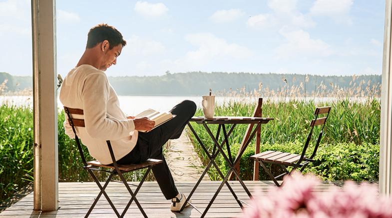 Ein junger Mann sitzt auf seiner Terrasse und liest ein Buch.
