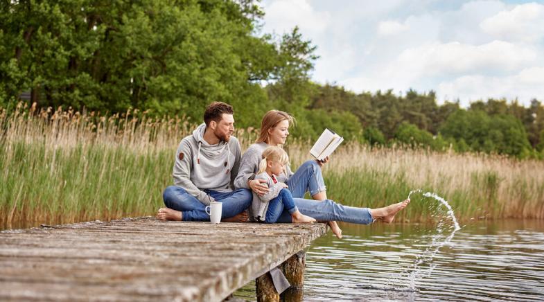 VRK Risiko-Lebensversicherung – Eine junge Familie sitzt zusammen auf einem Steg am See.