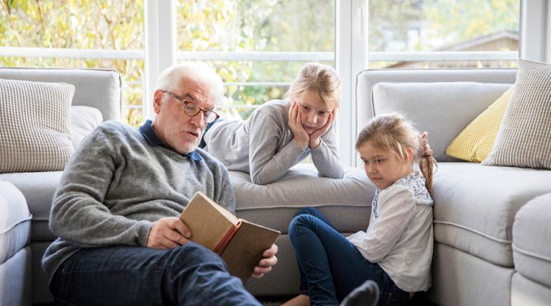 VRK Sterbegeldversicherung – Ein Opa liest seinen Enkeltöchtern eine Geschichte vor.