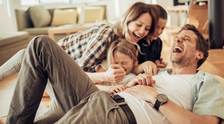VRK Unfallschutzbrief – Eine junge Familie lacht zusammen im Wohnzimmer.