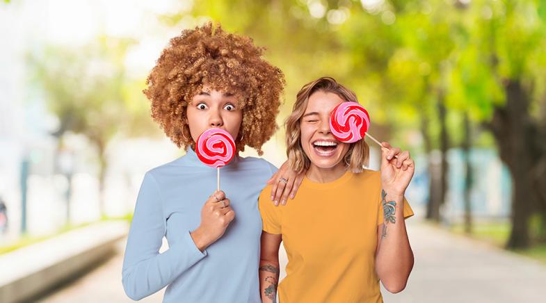 VRK Zahnzusatzversicherung – Zwei lachende junge Frauen mit Lutschern im Park.