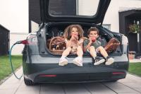 Elektroauto wird geladen, Kinder sitzen im Kofferaum