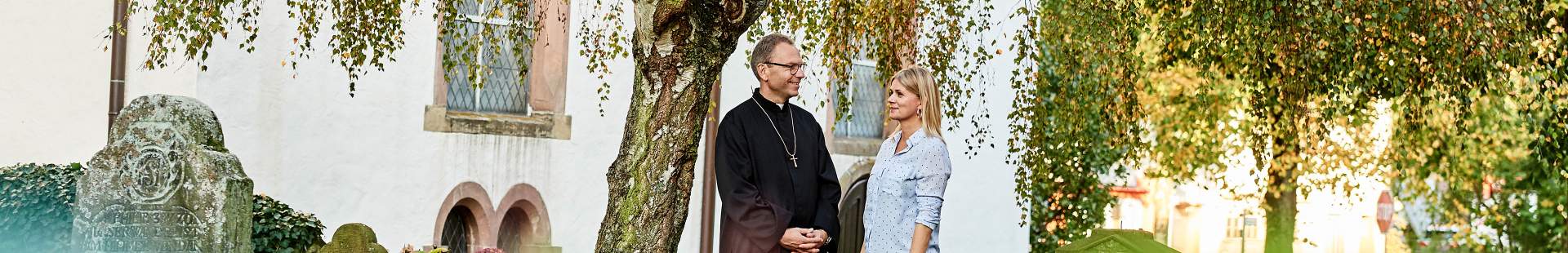 VRK Amts- und Vermögensschaden-Haftpflichtversicherung – Ein Kirchenbeamter steht mit einer Frau vor einem Kirchengebäude.