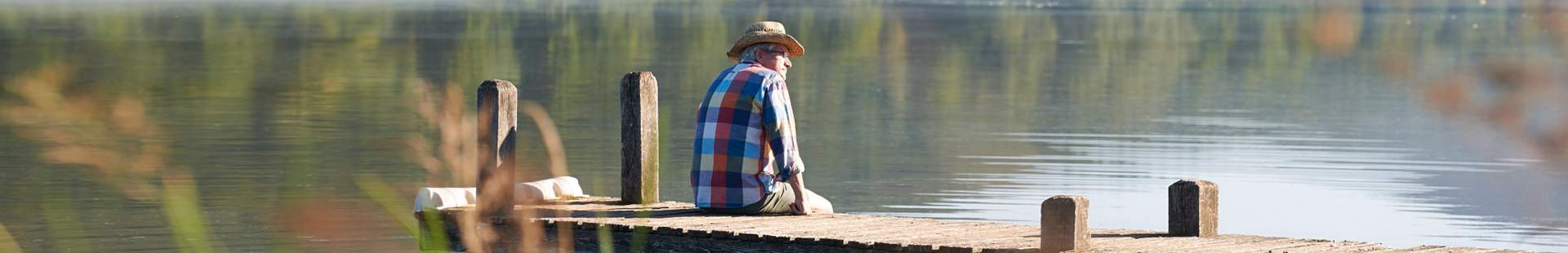VRK Rürup Rente – Alter Mann sitzt auf einem Holzsteg am See.