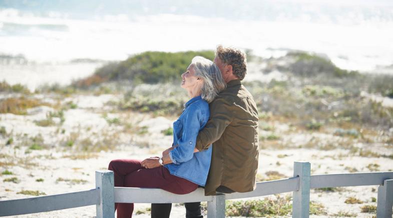 VRK Sofortrente – Ein älteres Ehepaar sitzt gemeinsam auf einem Zaun in den Dünen am Strand.